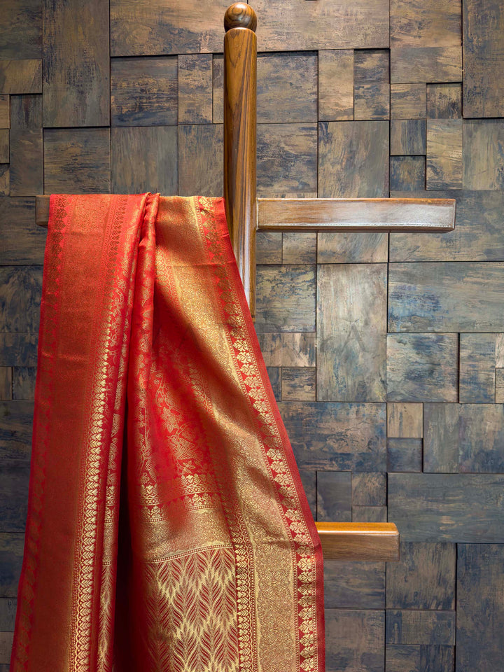 Close-up of red saree border featuring layered gold zari and floral vines.  Red saree with gold patterns hanging on a wooden hanger against a textured wall.