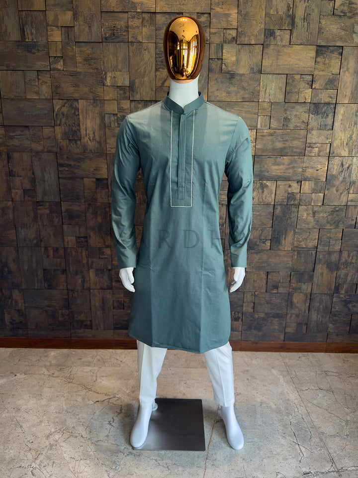 Mannequin wearing a green kurta with a gold mask against a wooden paneled wall. Modern minimalist men’s ethnic wear: A Slate Green cotton kurta with clean architectural tailoring and a smooth, crisp drape.