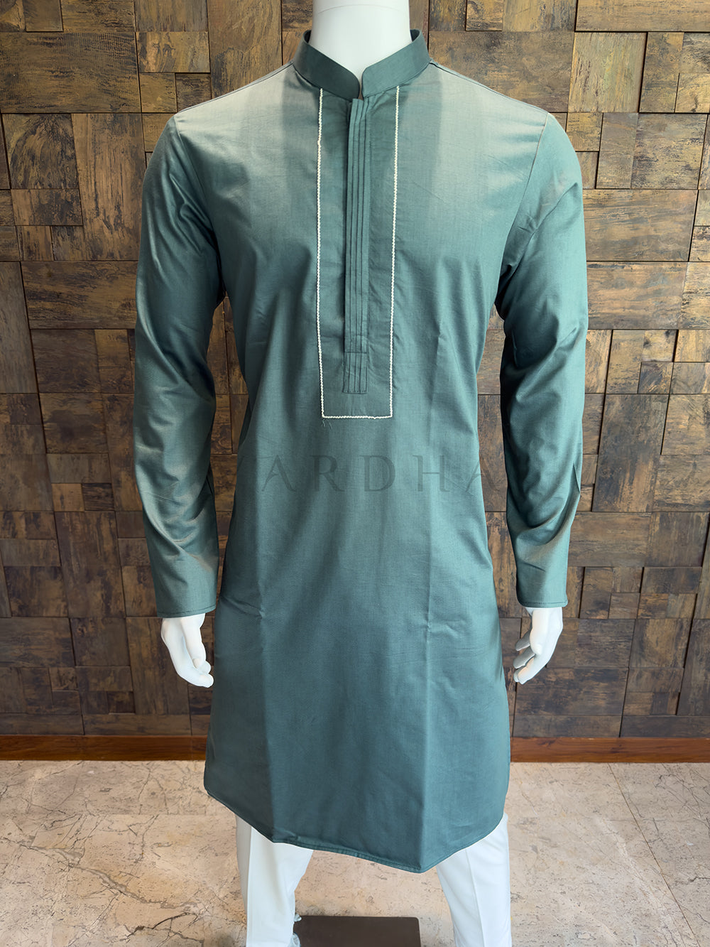 Green kurta on a mannequin against a wooden paneled wall. Premium breathable Slate Green cotton kurta for men, highlighting the smooth fabric finish and refined, uninterrupted tailoring.