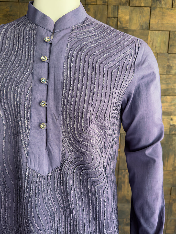 Purple embroidered shirt on a mannequin against a wooden wall background. Detailed chest view of the premium rhinestone buttons and the intricate cording on the mandarin collar of the grey designer kurta. Elegant men&