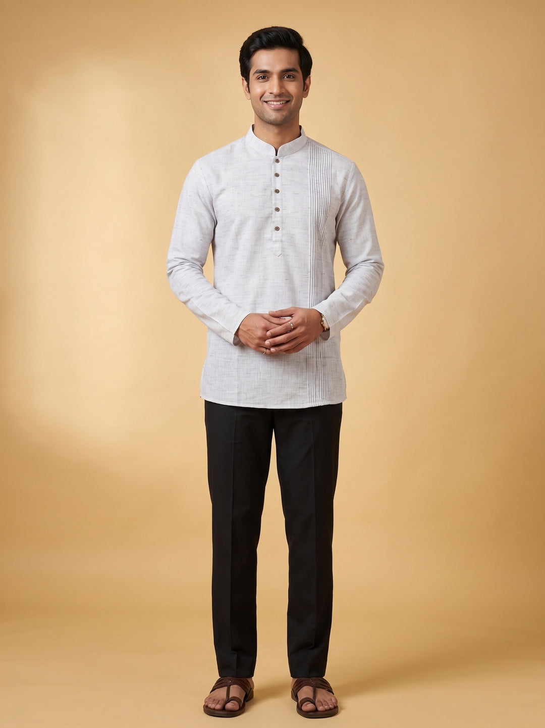 A man wearing a light gray textured long-sleeve kurta with a mandarin collar and black trousers, standing against a solid beige studio background. Full-length front view of a man modeling a steel grey cotton short kurta with a structured pintuck yoke, paired with black trousers.