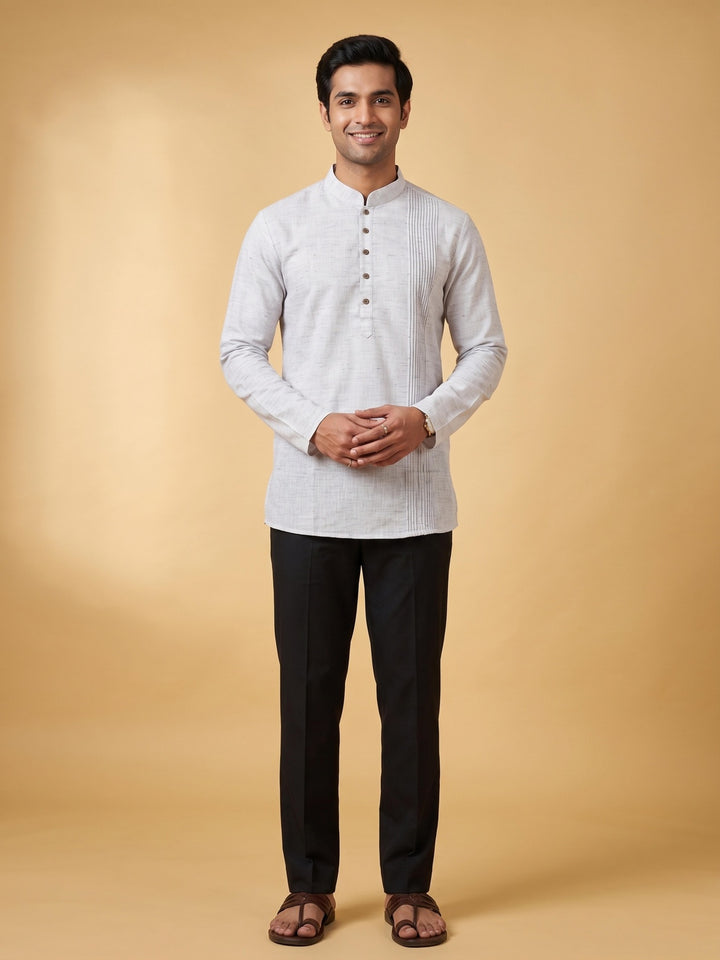 A man wearing a light gray textured long-sleeve kurta with a mandarin collar and black trousers, standing against a solid beige studio background. Full-length front view of a man modeling a steel grey cotton short kurta with a structured pintuck yoke, paired with black trousers.