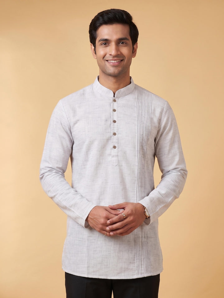 A man wearing a light gray long-sleeve kurta with a mandarin collar and button placket, standing against a solid beige background. Close-up front view of a man wearing a steel grey cotton short kurta with a structured pintuck yoke and buttoned placket.