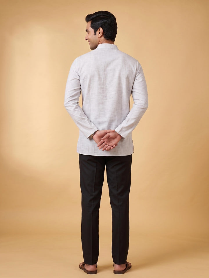 A man shown from the back wearing a light gray long-sleeve kurta and black trousers, standing against a solid beige studio background. Back view of a man showcasing the fit and length of a steel grey cotton short kurta paired with black trousers.