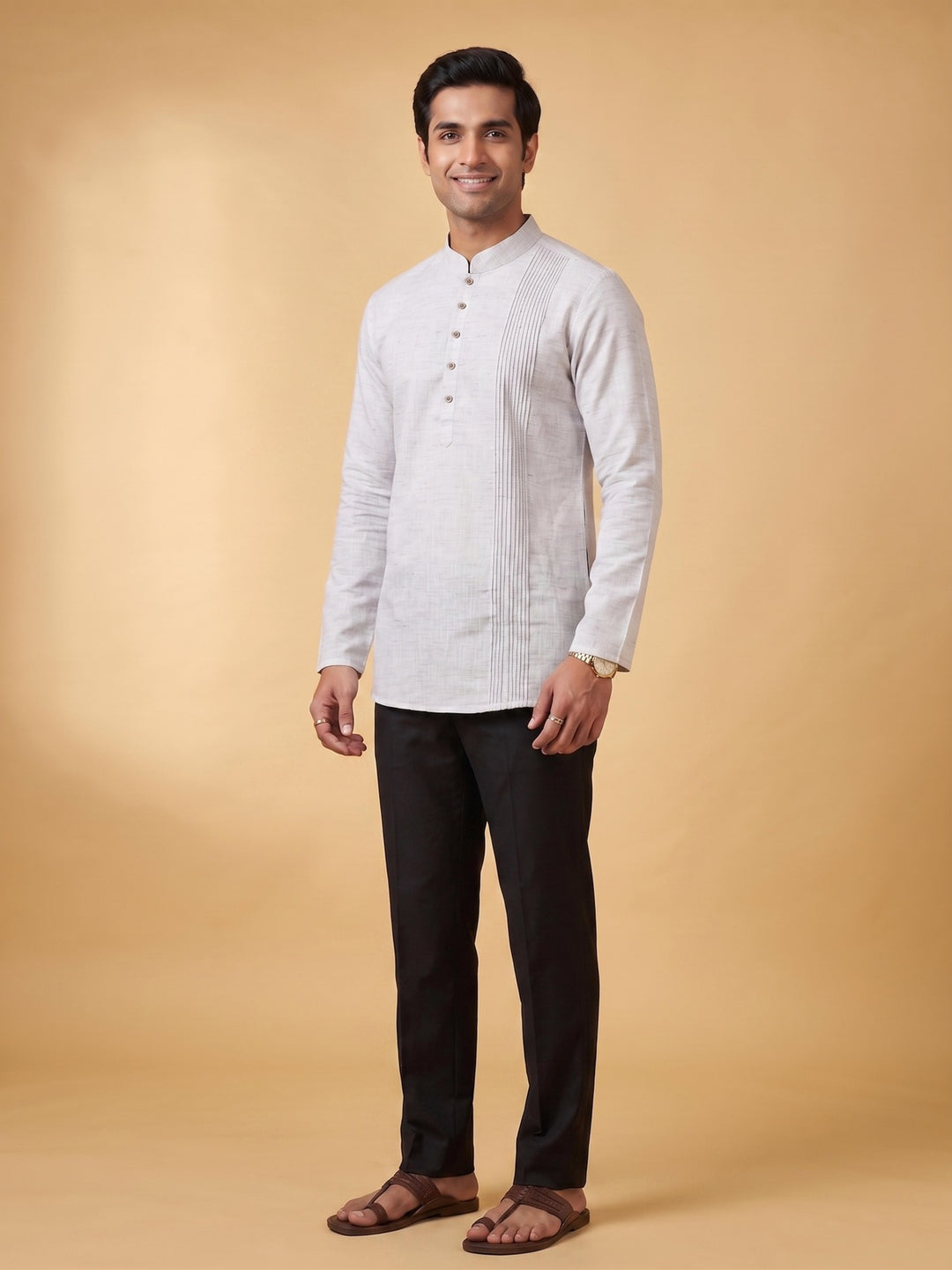 A man modeling a white long-sleeve kurta with a mandarin collar and front buttons, paired with black trousers and brown sandals, against a solid beige studio background. A man standing in a steel grey cotton short kurta with a structured pintuck yoke, showcasing a smart casual look.