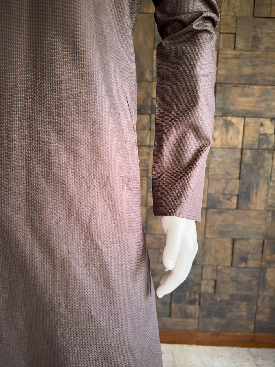 Mannequin wearing a brown textured garment against a wooden paneled wall. Close-up of the full sleeve and side drape of the textured brown cotton kurta, showcasing the breathable premium fabric and clean, elegant contemporary aesthetic.