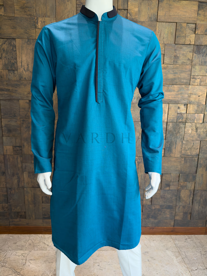 Blue kurta on a mannequin against a wooden paneled wall. Sophisticated Teal Blue cotton kurta with contrast detailing; a refined ethnic piece that pairs exceptionally well with white or cream pyjamas.