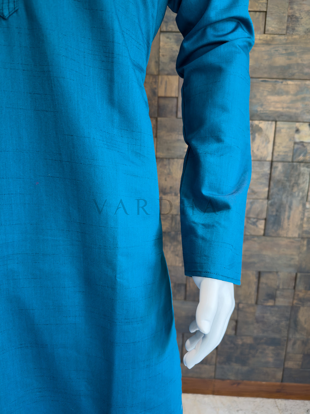 Blue garment on a mannequin with a wooden floor background. Elegant jewel-toned Teal Blue kurta for men, designed for evening receptions and festive gatherings, featuring full sleeves and a formal finish.