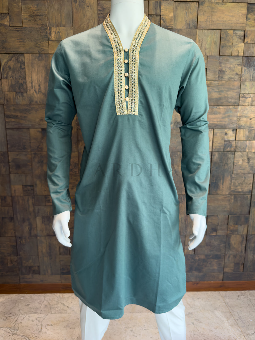 teal blue kurta with gold embroidery on a mannequin against a wooden wall. Elegant Teal Blue designer kurta for festive brunches and morning pujas, featuring a regal yet understated aesthetic with full sleeves.