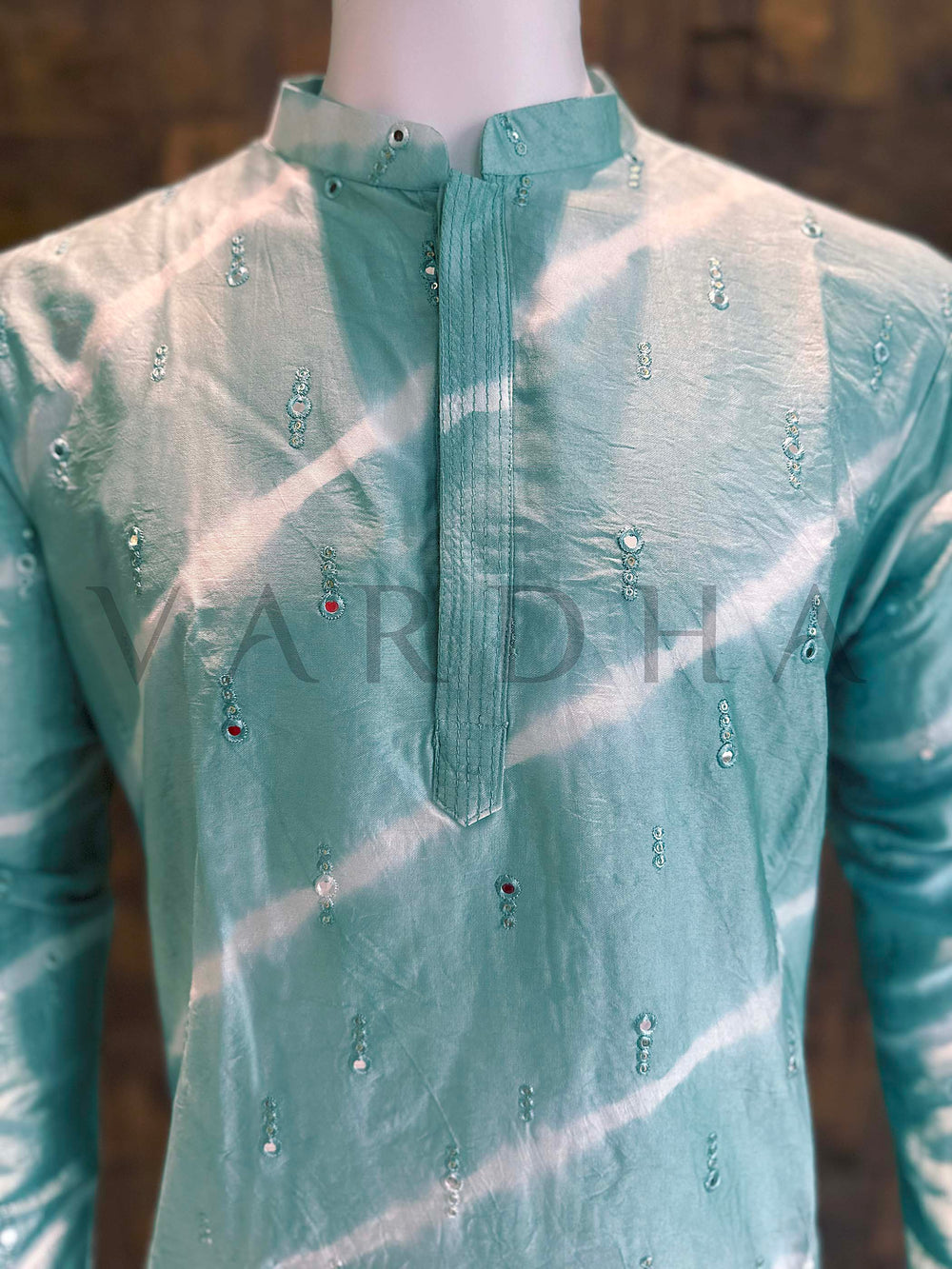 Green embroidered shirt on a mannequin with a blurred background Close-up of mint teal kurta neckline showing neat band collar, clean concealed placket and refined mini-sequin clusters on smooth viscose fabric.