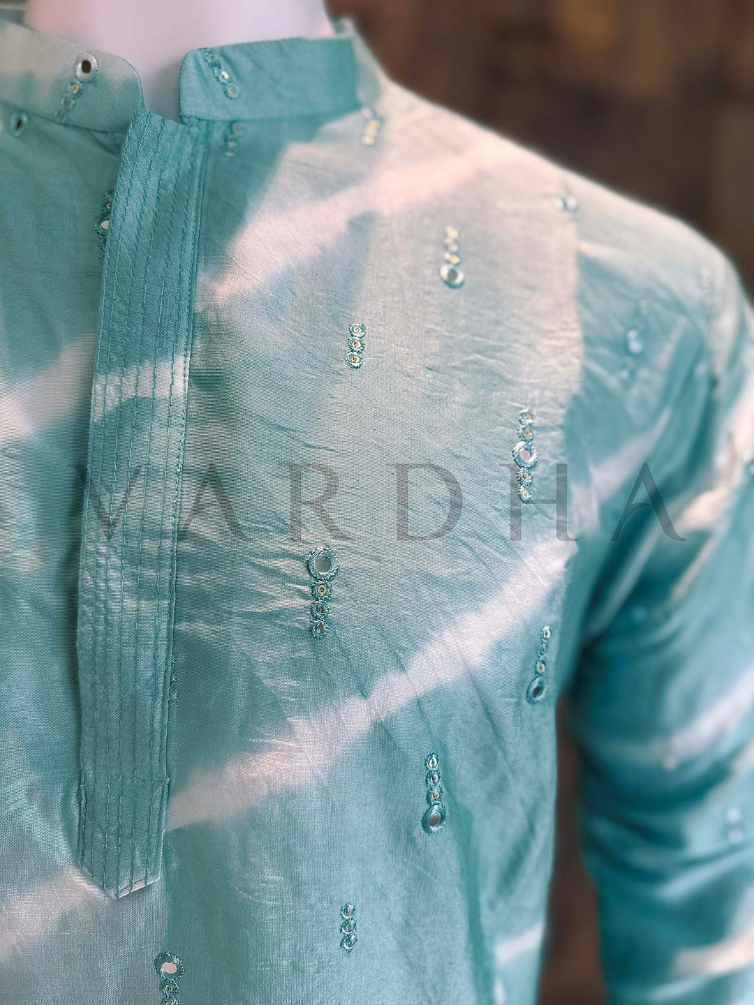 Green embroidered shirt with 'Vardha' branding on a blurred background Angled shot emphasizing slimming diagonal bands, crisp collar construction and elegant concealed placket on lightweight viscose kurta.
