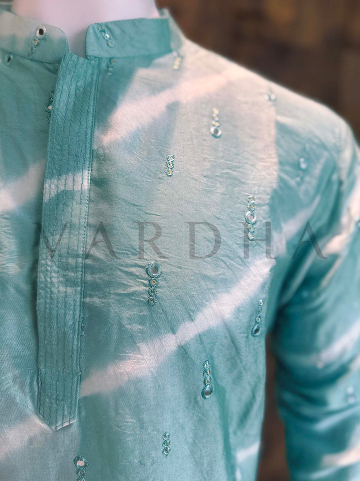 Green embroidered shirt with 'Vardha' branding on a blurred background Angled shot emphasizing slimming diagonal bands, crisp collar construction and elegant concealed placket on lightweight viscose kurta.