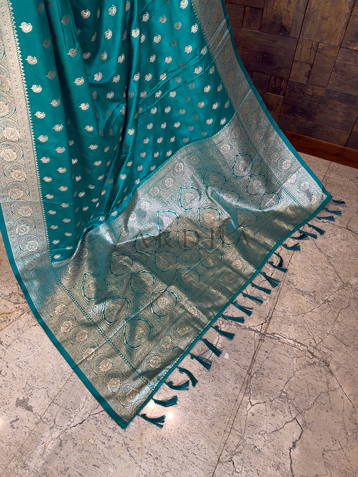 Teal saree with white patterns on a stone floor Detailed floor view of the rich, densely woven zari pallu with matching tassels on a vibrant sea green satin saree.