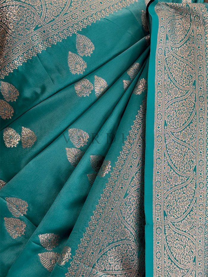 Teal saree with silver leaf patterns and border Festive ethnic wear teal zari woven saree sweeping the floor, showcasing the heavily brocaded pallu and traditional patterns. Rich Indian wedding guest attire featuring a teal green satin saree with opulent paisley pallu details and border.