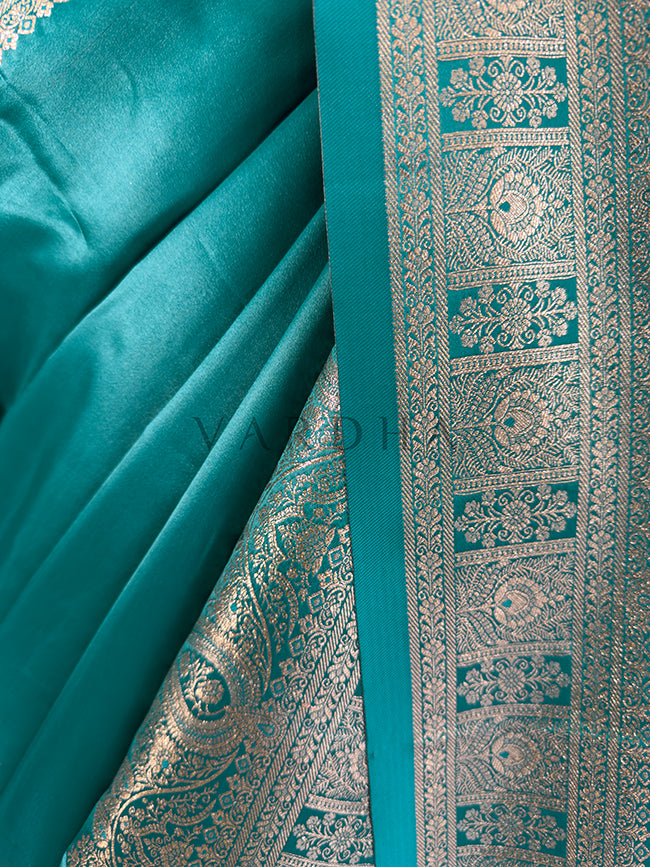 Teal fabric with intricate gold patterns Close-up texture shot highlighting the solid glossy teal fabric contrasting with the intricate geometric floral zari border. Elegant party wear teal satin silk saree highlighting its smooth drape, lustrous shine, and exceptional zari craftsmanship. Rich Indian wedding guest attire featuring a solid teal green satin saree with opulent border details and traditional metallic weaving.