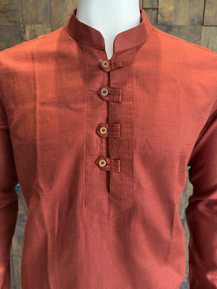 Orange kurta on a mannequin against a wooden panel background. Close-up of a designer rust orange kurta showing the distinct micro-check fabric pattern and rustic, artisanal wooden-style buttons.