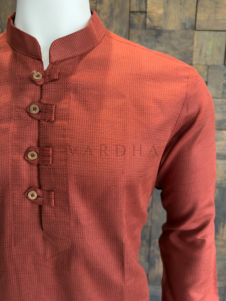 Orange kurta shirt on a mannequin with a textured pattern against a stone wall background. Terracotta Orange Designer Cotton Kurta for Men - Micro-Check Textured Ethnic Wear for Haldi.
