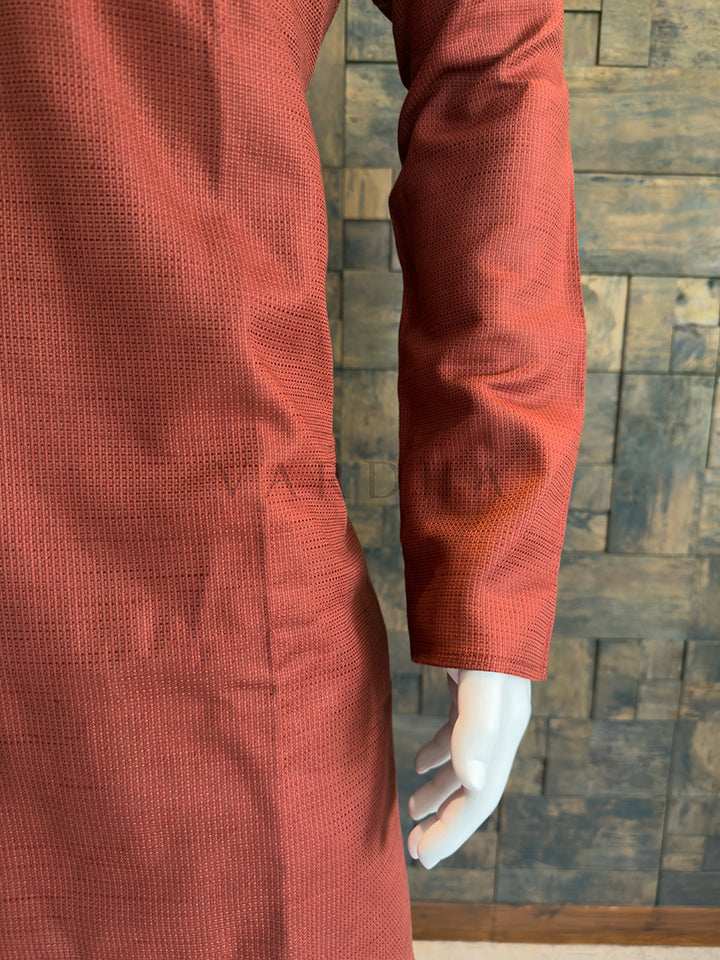 Orange textured coat worn by a person against a wooden paneled wall. Men’s terracotta orange kurta highlighting the artisanal tailoring, including a functional extended placket with fabric tabs and full sleeves.