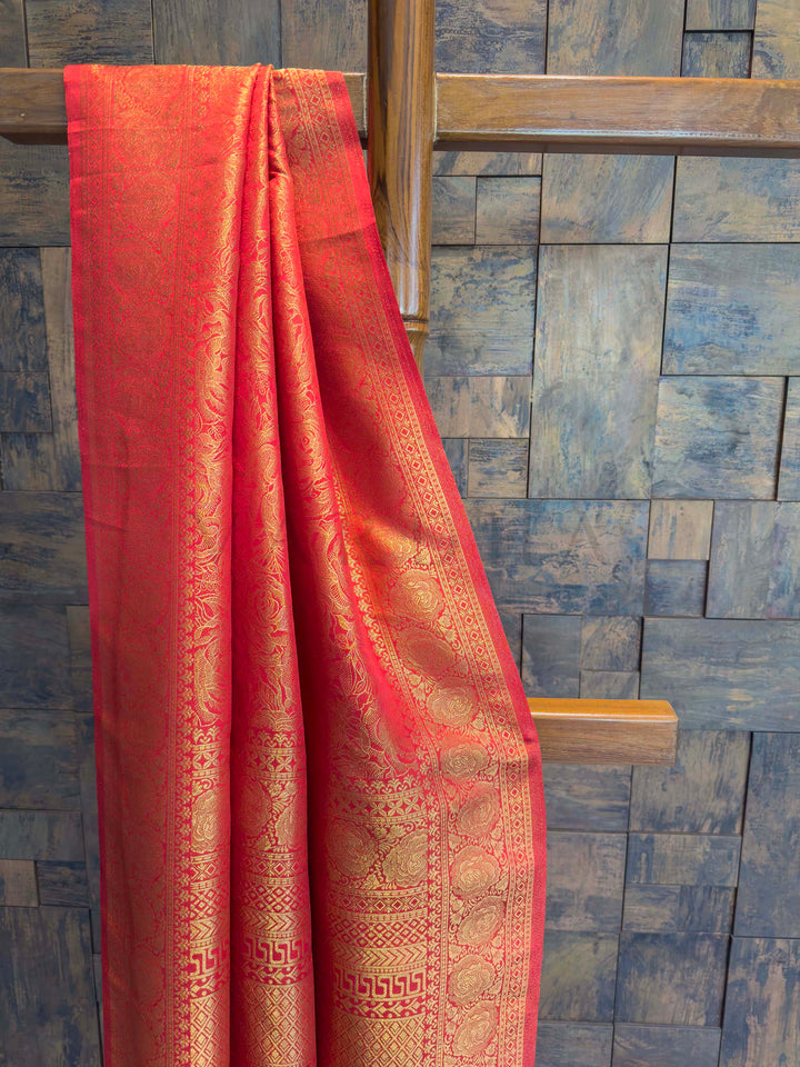 Red fabric with gold patterns draped over a wooden rod against a blue tiled wall. Close-up of broad red border featuring circular and geometric gold zari patterns