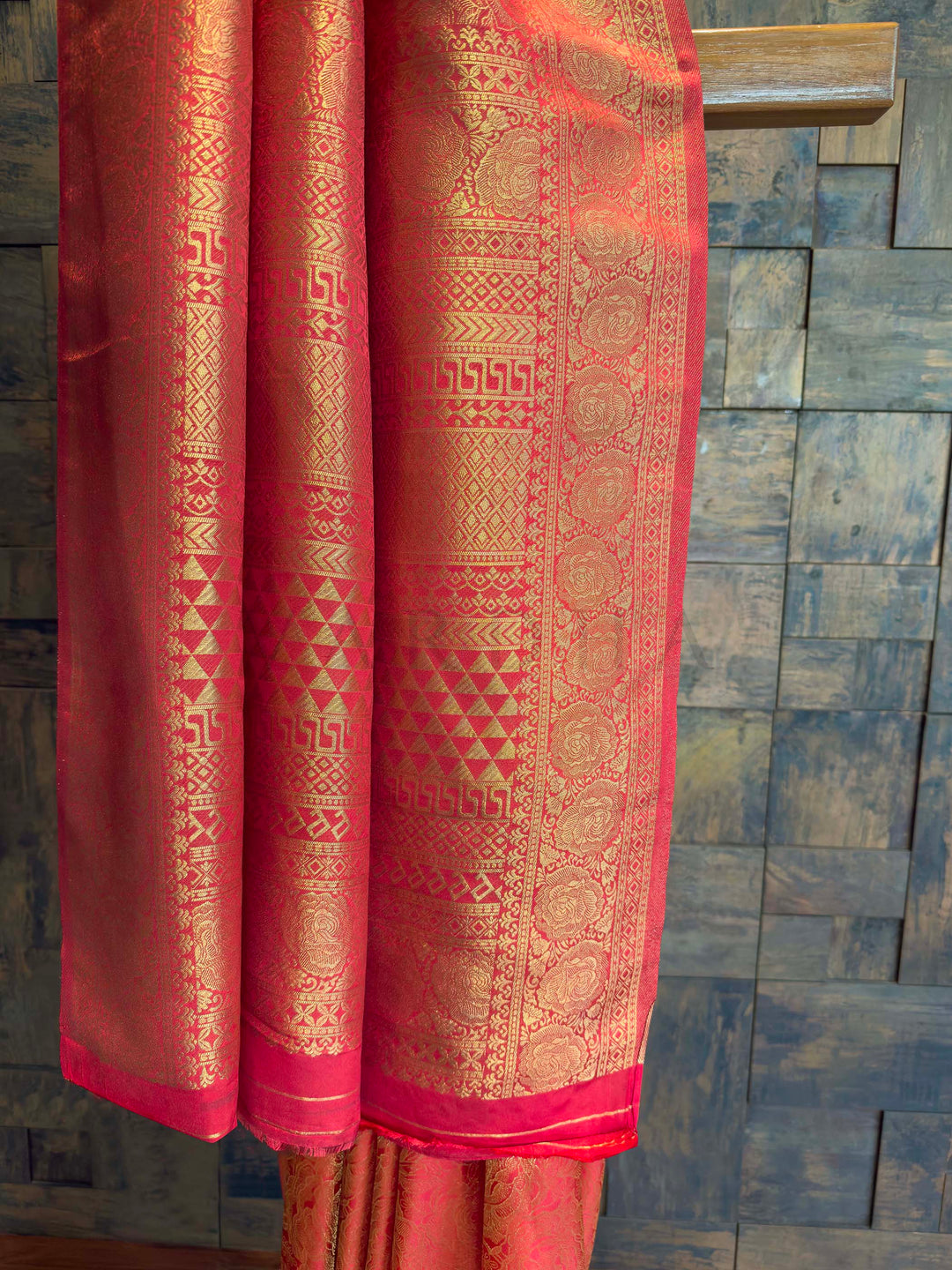 Red saree with gold patterns draped over a wooden surface Rich gold zari pallu with traditional floral and geometric motifs