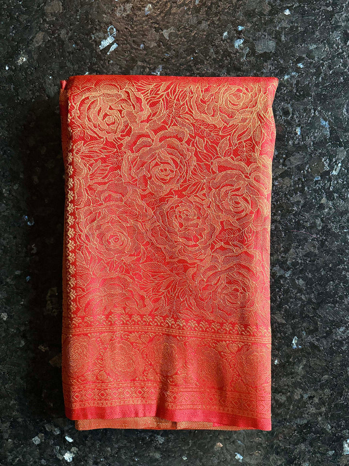 Red embroidered fabric on a dark textured surface Detailed view of floral and geometric gold zari weaving on red Kanjivaram fabric