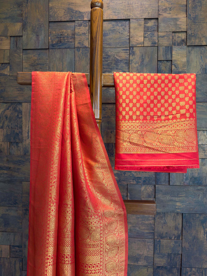 Red saree with gold patterns draped over a wooden rod against a textured blue wall. Close shot of gold zari craftsmanship on red saree body and border