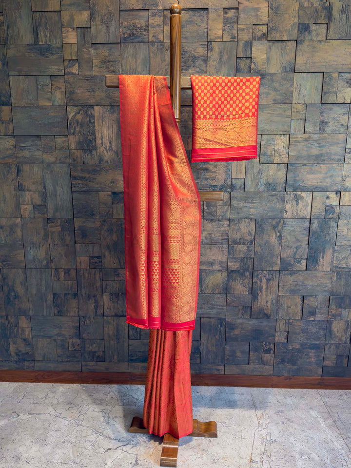 Red saree with gold patterns on a wooden stand against a textured wall. Full-length drape of vermilion red golden zari Kanjivaram saree on wooden stand