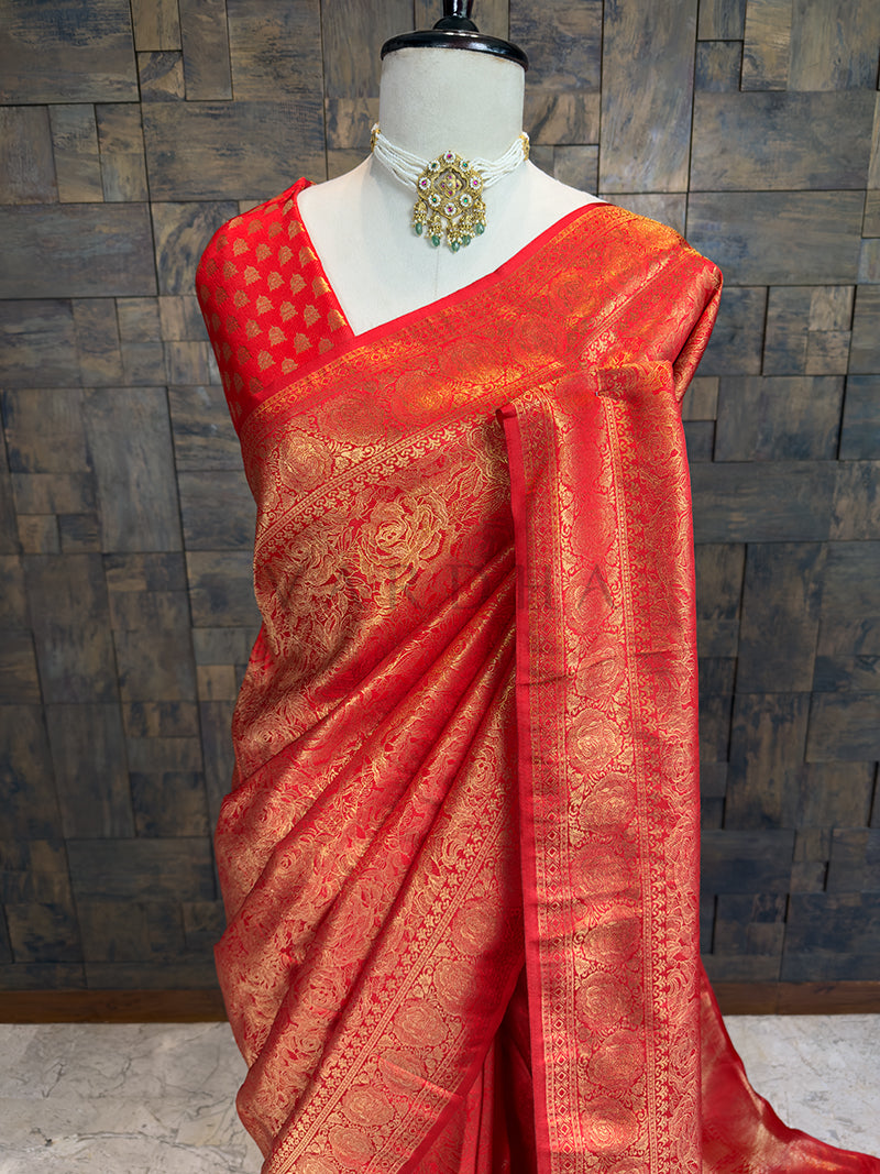 Elegant copper-red festive saree by House of Vardha featuring intricate traditional gold woven floral motifs. Red saree with gold patterns on a mannequin against a textured wall.