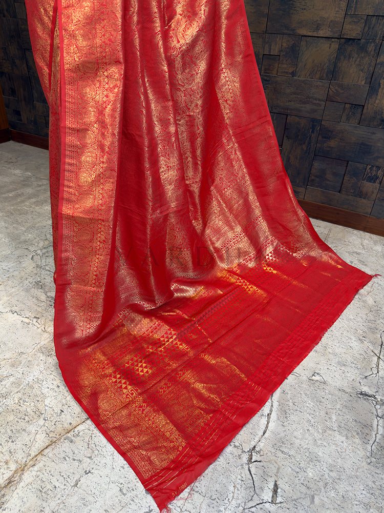 Luxurious Indian bridal saree in a deep pink-red tone from House of Vardha with heavy gold zari embellishments. Red fabric with gold patterns draped over a stone surface
