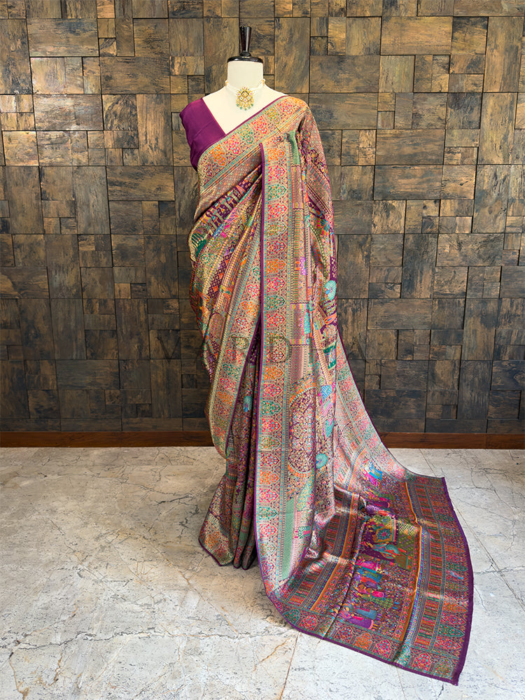 Colorful saree with a mannequin against a wooden paneled wall. Full-length view of a luxurious deep purple silk saree draped on a mannequin, featuring intricate multi-colored Meenakari weaving, geometric diamond patterns, and heavy traditional borders. Perfect for Indian bridal wear and grand festive occasions.