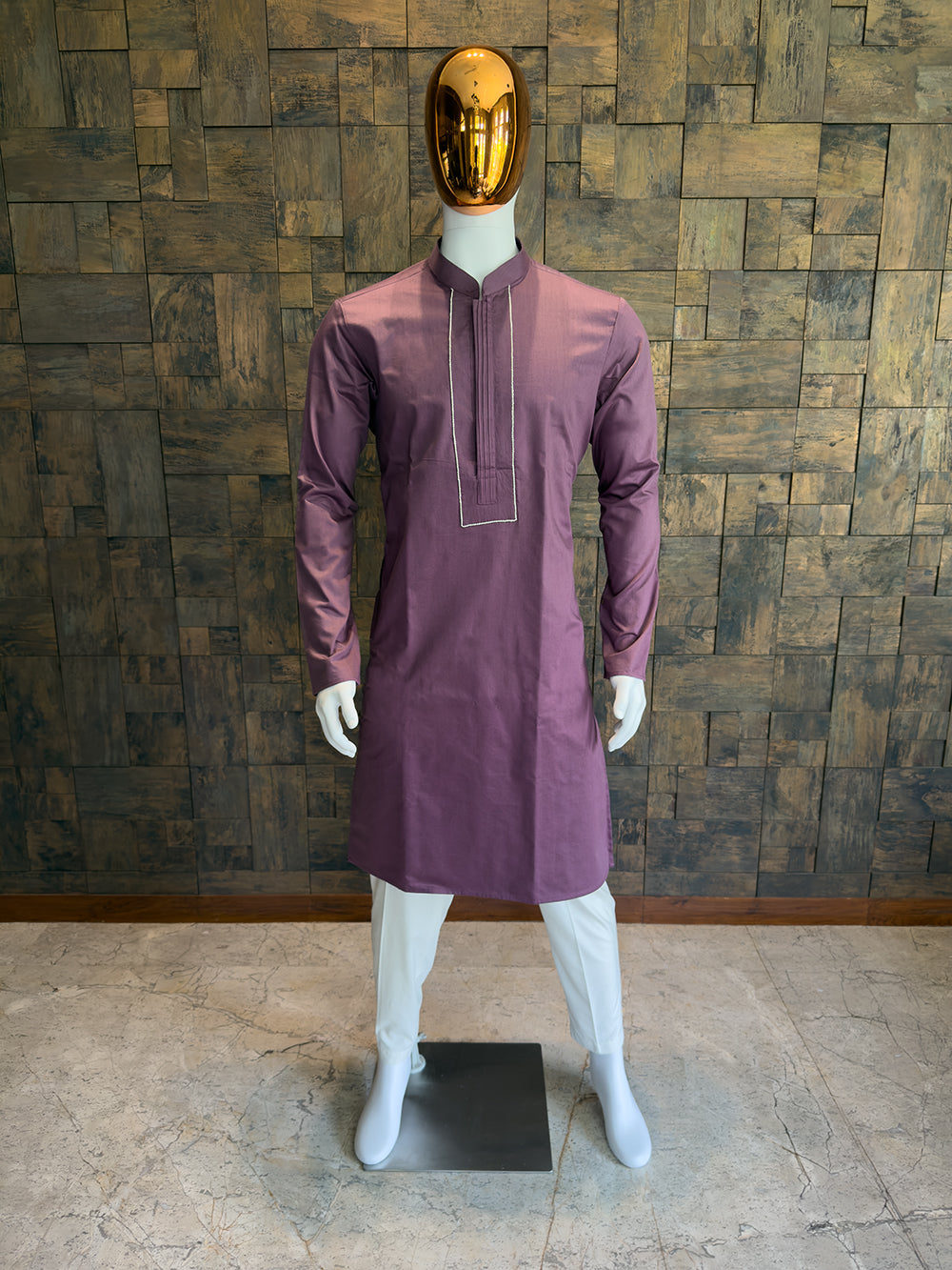 Mannequin wearing a purple kurta with a gold mask against a wooden paneled wall. Close-up of a Wine designer kurta showing the seamless concealed button placket framed by a sharp, contrasting rectangular stitched border.