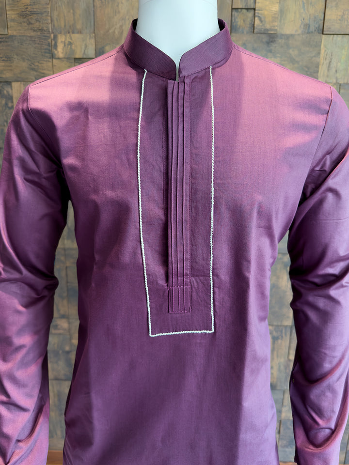 Purple kurta with white embroidery on a wooden background. Modern minimalist men’s ethnic wear: A knee-length Wine cotton kurta with clean architectural tailoring and a smooth, polished drape.