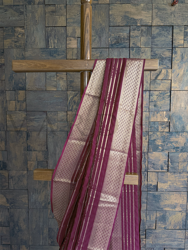 Detailed diamond jaal trellis weave in gold zari on wine georgette saree, paired with striped pallu for elegant finish
