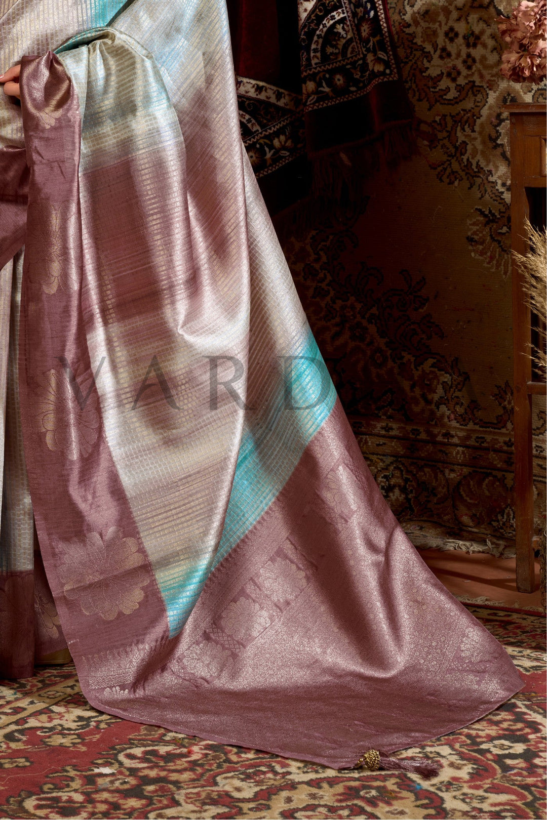 Purple saree with blue border draped over a chair in a room with patterned carpet Enjoy premium add-ons including Pre-drape Services, Custom Stitched Blouse at a Complimentary Price, Fall and Edging, Gift Packaging, and Free Shipping!