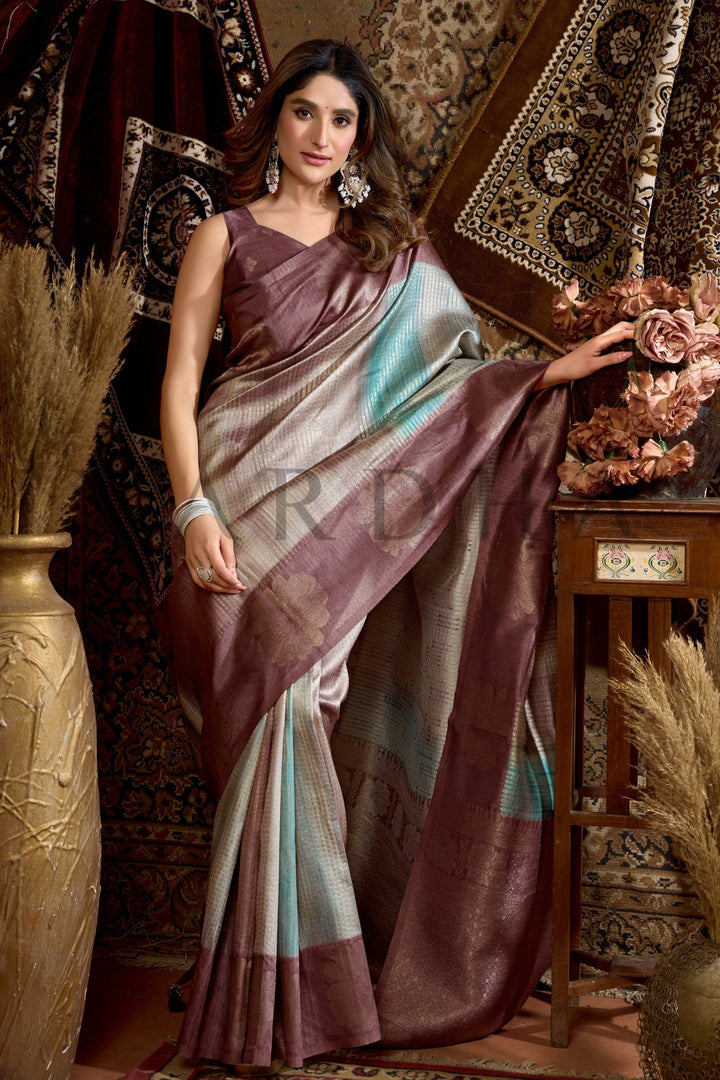 Woman in a traditional saree standing in an ornate room with decorative elements. Enjoy premium add-ons including Pre-drape Services, Custom Stitched Blouse at a Complimentary Price, Fall and Edging, Gift Packaging, and Free Shipping!