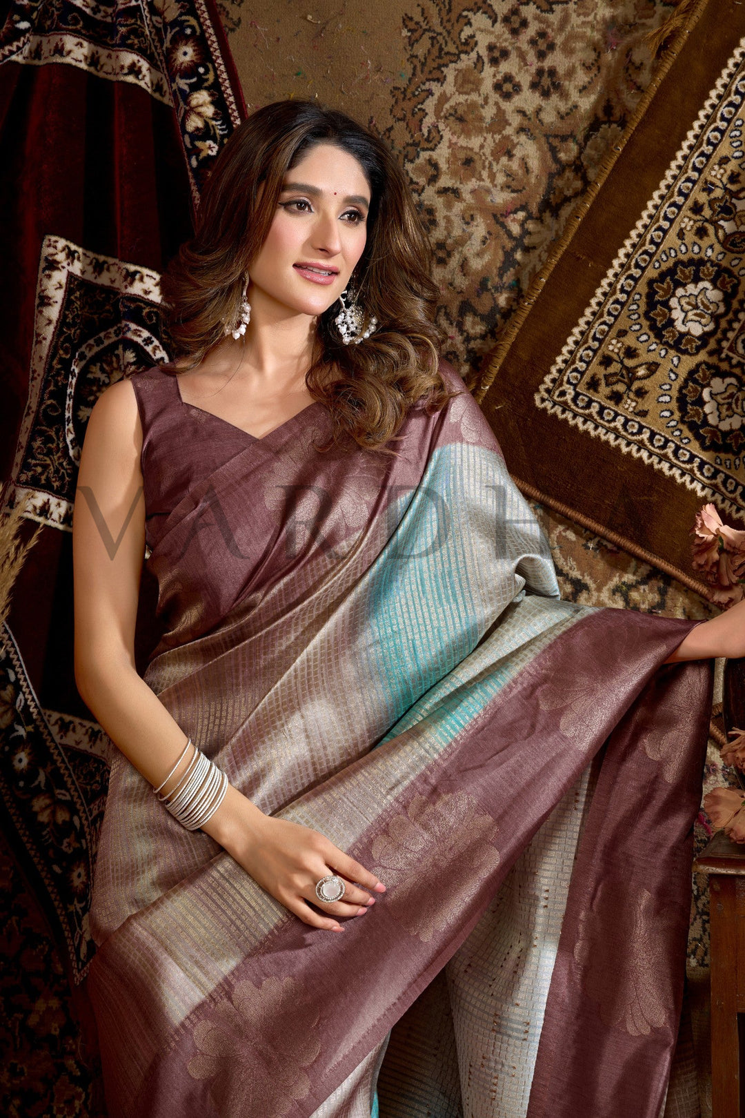 Woman wearing a traditional saree in a decorative setting Dual-tone metallic finish with traditional woven floral bootas and a geometric striped pallu