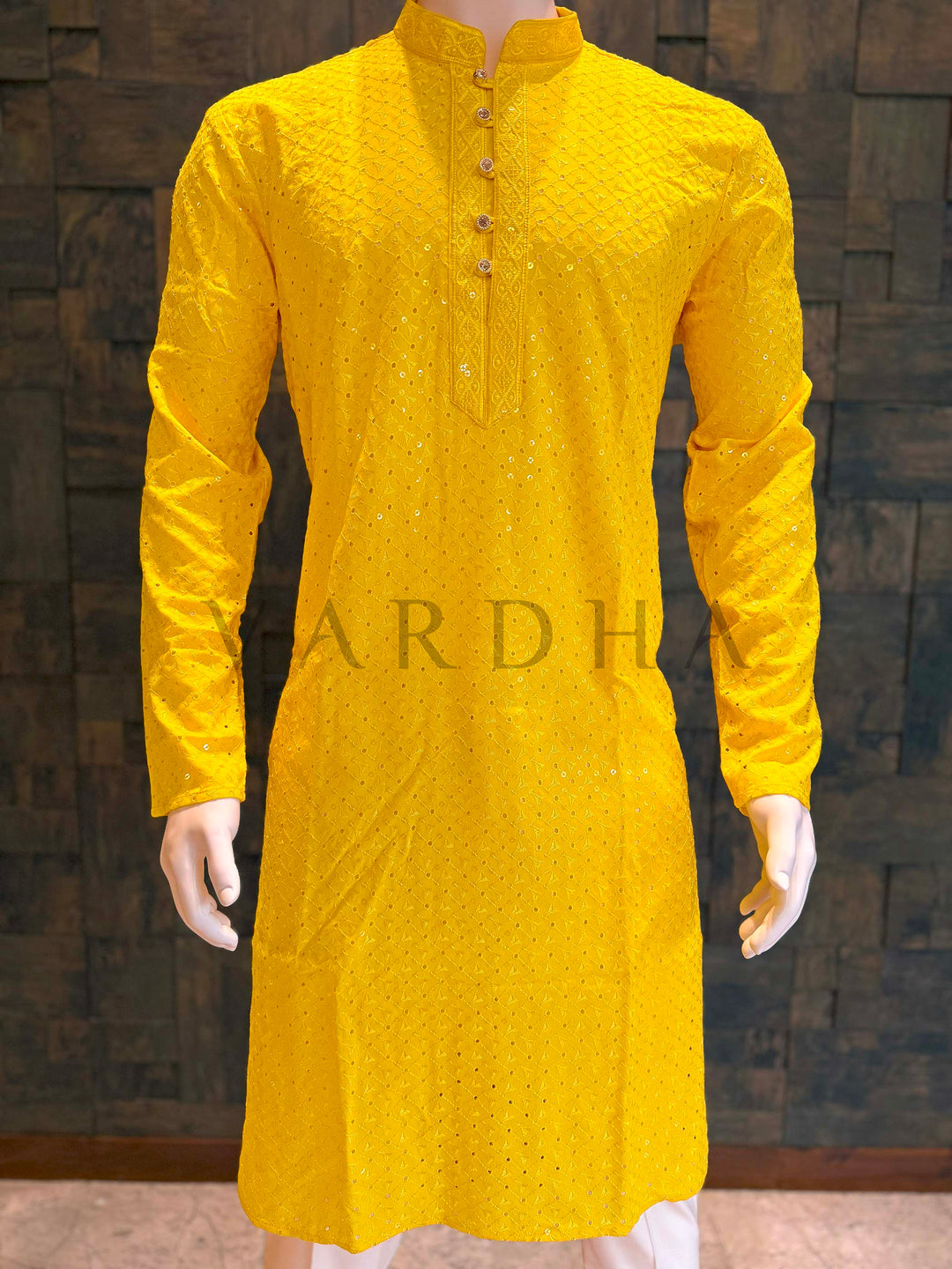Yellow kurta on a mannequin against a dark textured wall Front chest detail of marigold kurta highlighting woven lattice texture, delicate sequin sparkle and refined placket construction for weddings and sangeet.