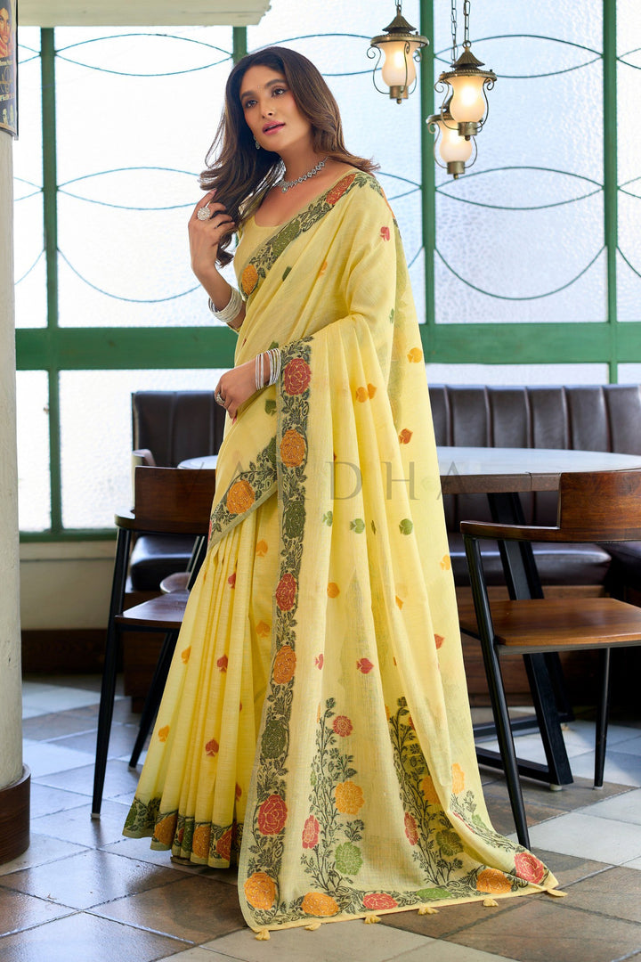 Woman in a yellow saree with floral patterns in an indoor setting Elegant woman posing in a yellow linen party-wear saree, highlighting the beautiful fall, scattered body motifs, and traditional woven floral hem.