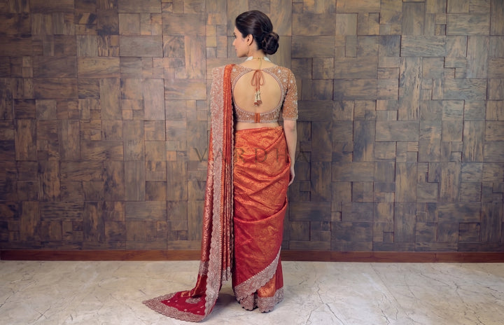 Woman in an red saree standing against a textured wall.