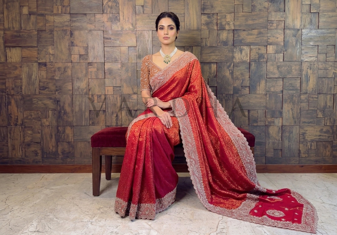 Woman in a red saree sitting on a bench against a wooden paneled wall.