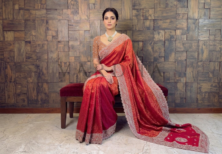 Woman in a red saree sitting on a bench against a wooden paneled wall.