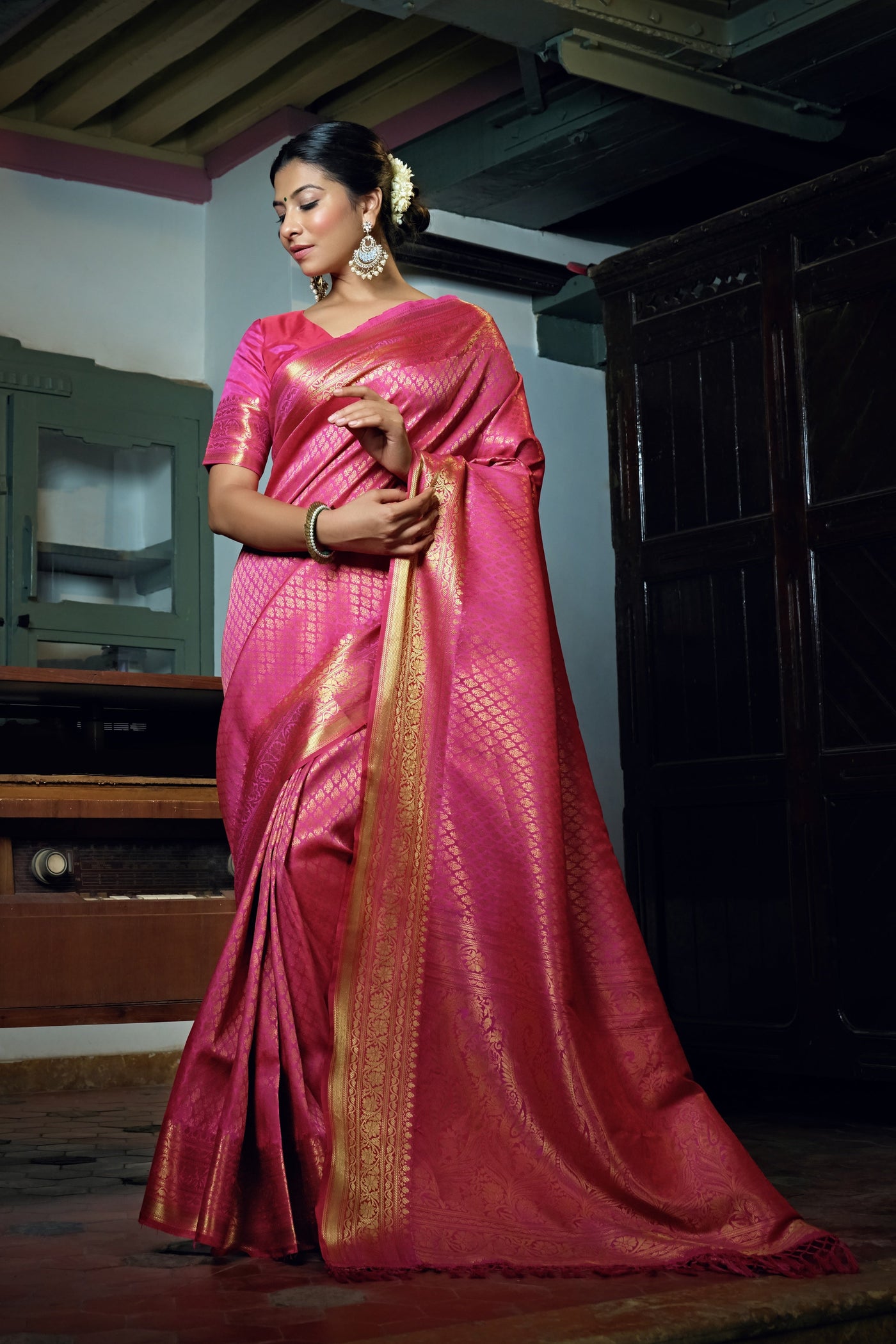 Model draped in a ruby pink Kanjeevaram saree showcasing gold zari buttas and a rich pallu.