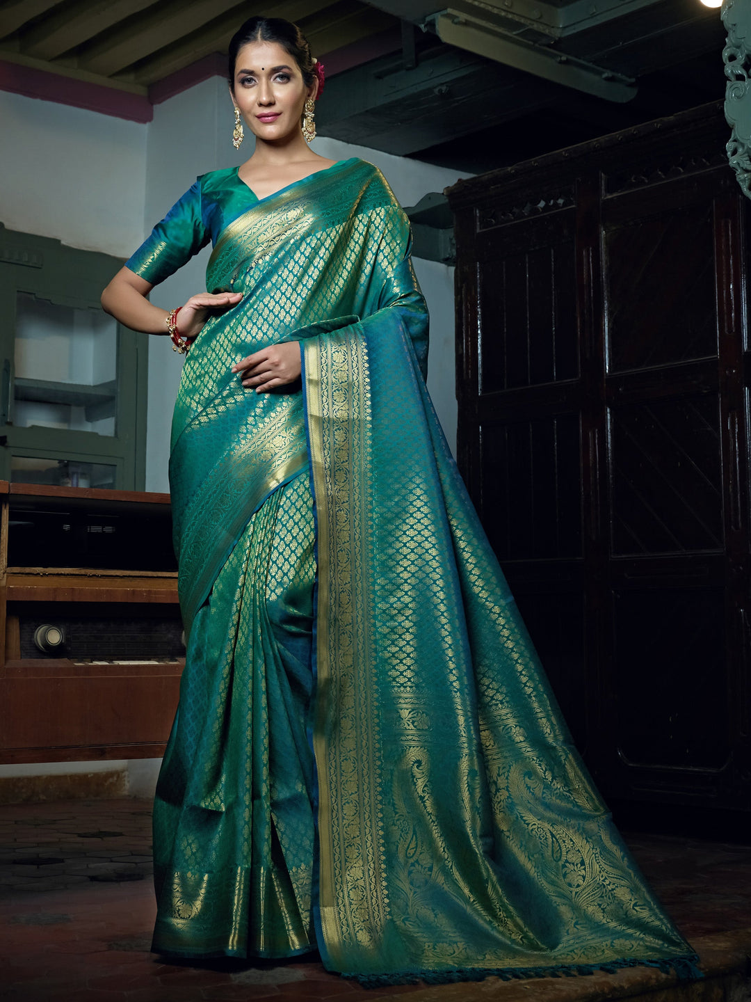 Model draped in Teal Blue Kanjivaram saree showcasing rich gold zari buttas and pallu design.